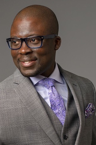 Photo 7 "The Strategist": gray suit jacket, lavender dress shirt, purple paisley tie and pocket square, dark-framed glasses, plain gray background